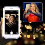 Woman taking a selfie at night with a bright city lights background.