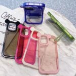 Transparent phone cases with colored borders and a green phone stand on a marble table.