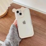 Clear iPhone case with bear ears held against wooden background.